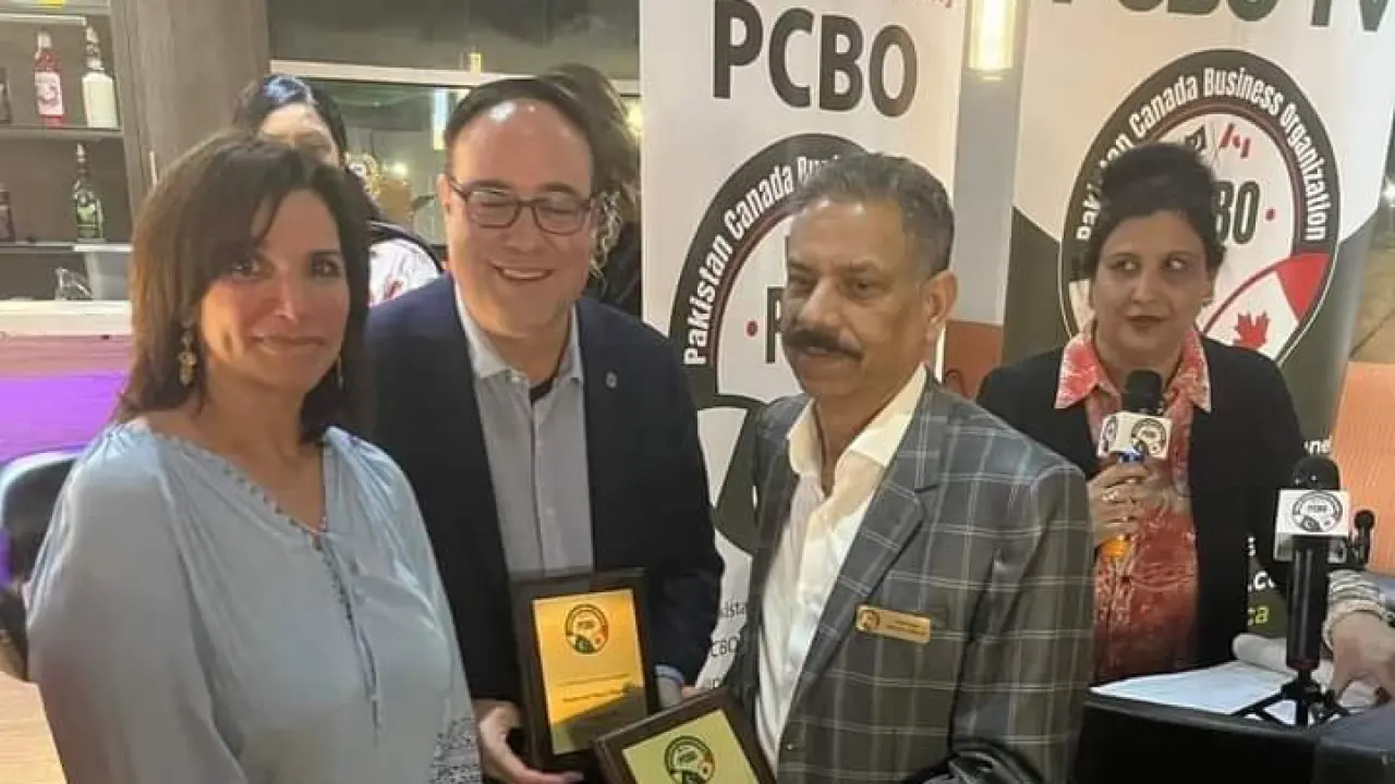 Two guests holding appreciation plaques beside the PCBO banner